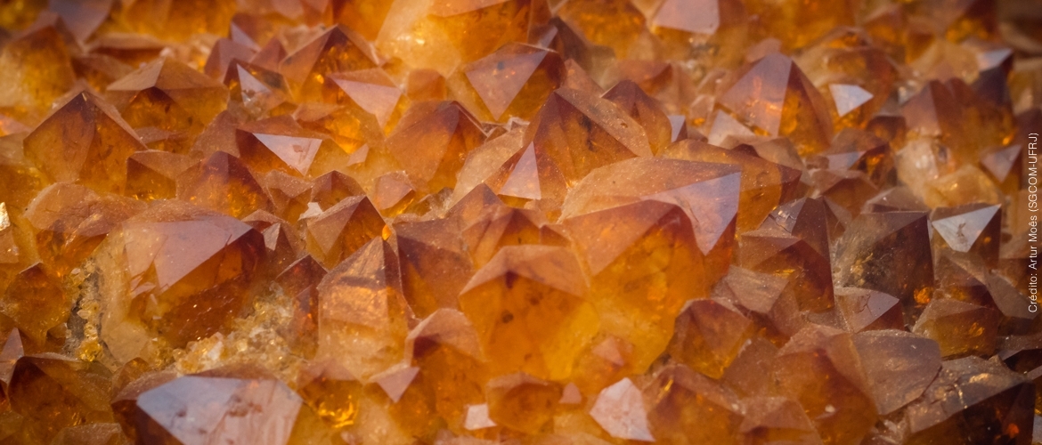 Foto em close de um citrino, que é alaranjado e tem cristais que lembram pirâmides.